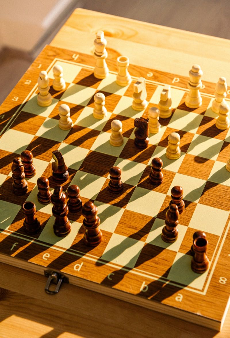 A chess game in progress on a wooden table beside two cups of tea
