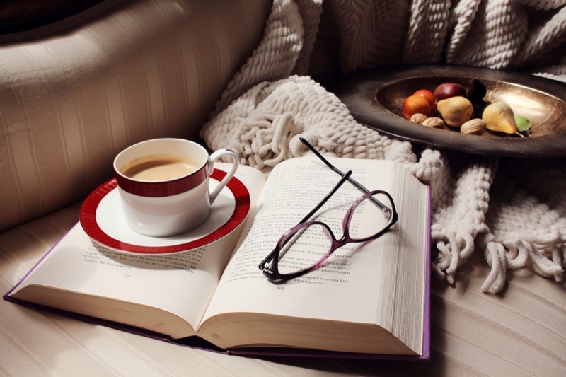 A cozy armchair with a blanket, open book, and cup of tea